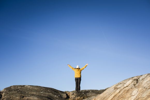 Person står på klippor och sträcker armarna mot blå himmel