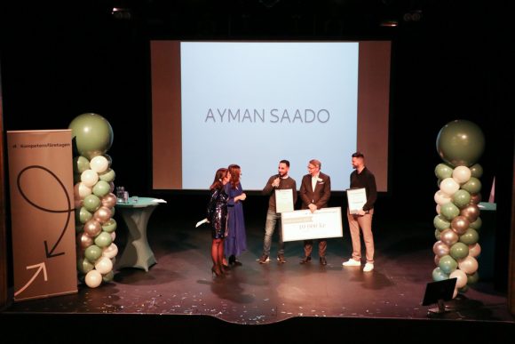 Årets konsult 2022 Ayman Saado intervjuas på scen med sitt namn på stor skärm bakom sig